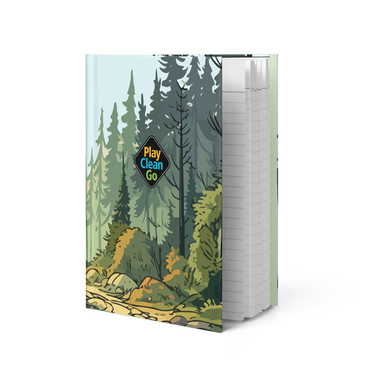 A hardcover notebook or journal standing upright, featuring a forest illustration on the cover with the words 'Play Clean Go' in a diamond-shaped badge. The pages are visible on the right side and are white with light gray horizontal lines.